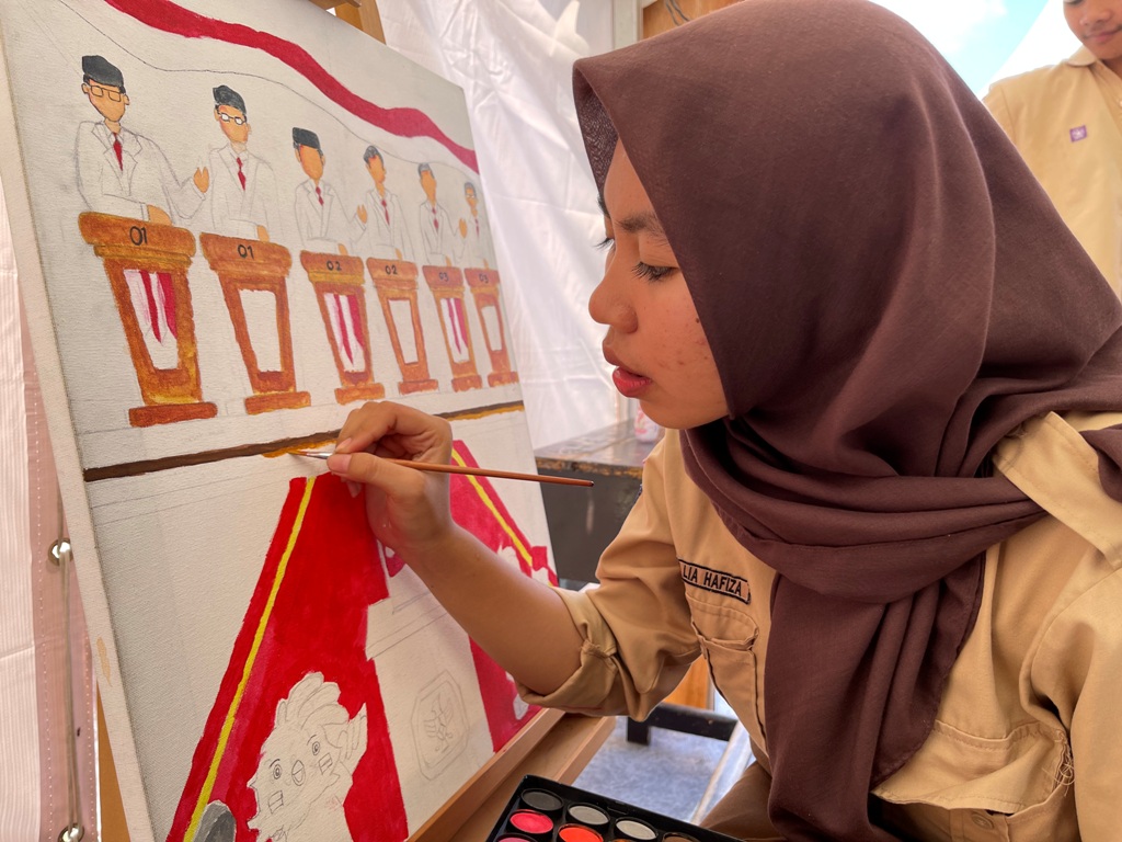 TEKUN: Agni Lia tengah menggambarkan apa yang muncul di pikirannya tentang Pilkada Serentak 2024 melalui karya lukisan, Sabtu (9/11).