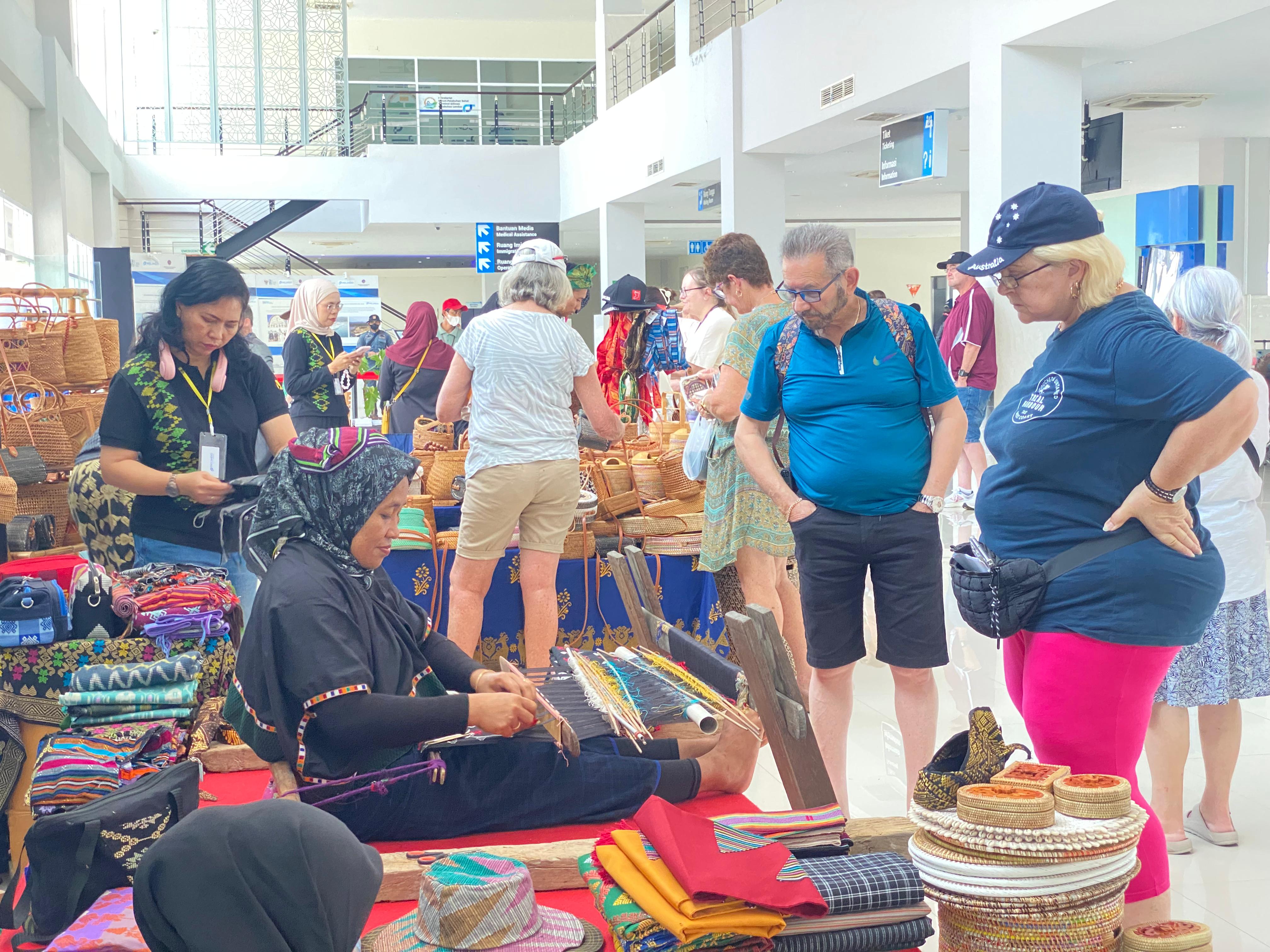 MELIHAT CARA MENENUN: Penumpang Quantum of the Seas Kapal Cruise melihat langsung proses menenun di Ruang Tunggu Pelabuhan Gilimas Lembar, Jumat (22/11). Pelindo For Lombok Post