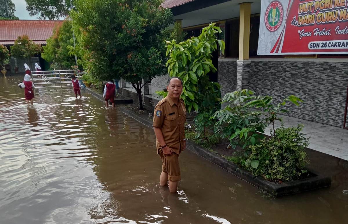 HARUS ADA SOLUSI: Murid dan guru SDN 26 Cakranegara melepas sepatu ke sekolah karena halaman terendam banjir, Selasa (10/12).