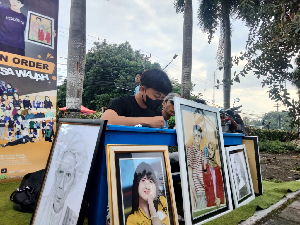 PUNYA KARYA: M Ali Assobuni saat melukis sekaligus memamerkan hasil karyanya untuk menarik mereka yang ingin digambar wajahnya di Taman Rinjani Selong, Senin (16/12).