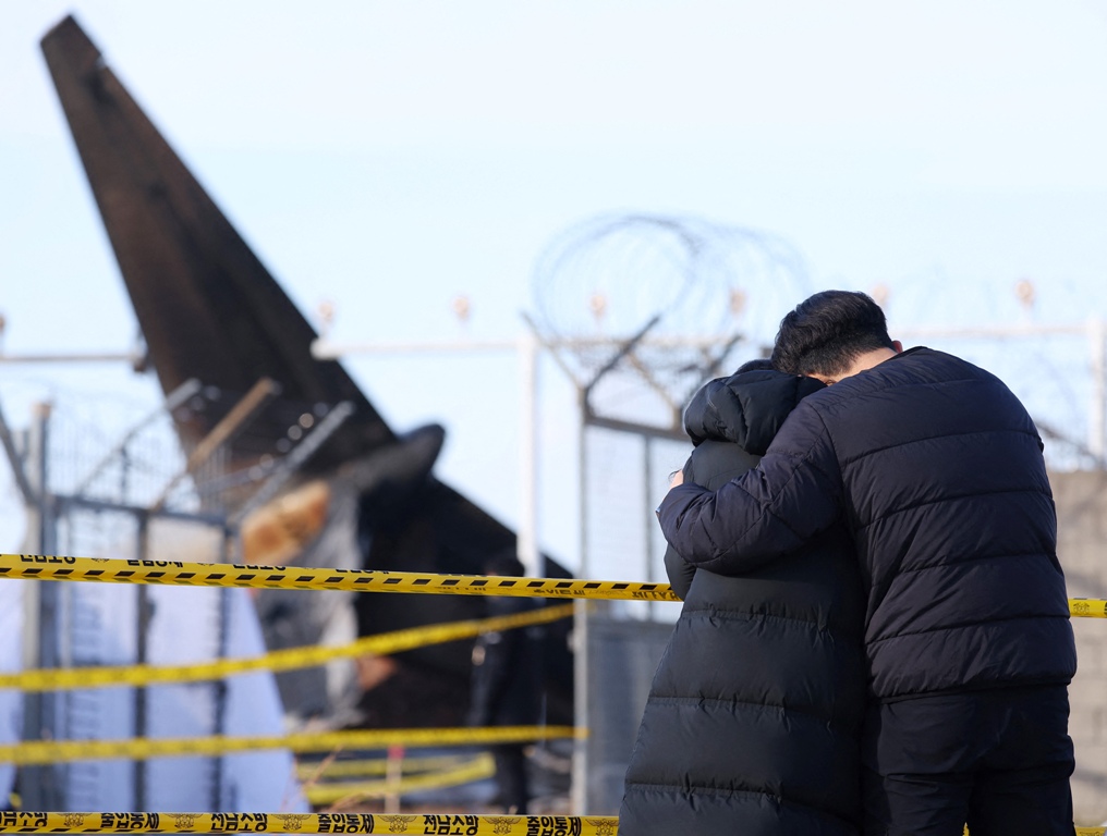 KELUARGA KORBAN: Anggota keluarga yang berduka berdiri di lokasi jatuhnya pesawat Boieng 737-800 Jeju Air dan terbakar di Bandara Internasional Muan, Korsel, Senin (30/12).