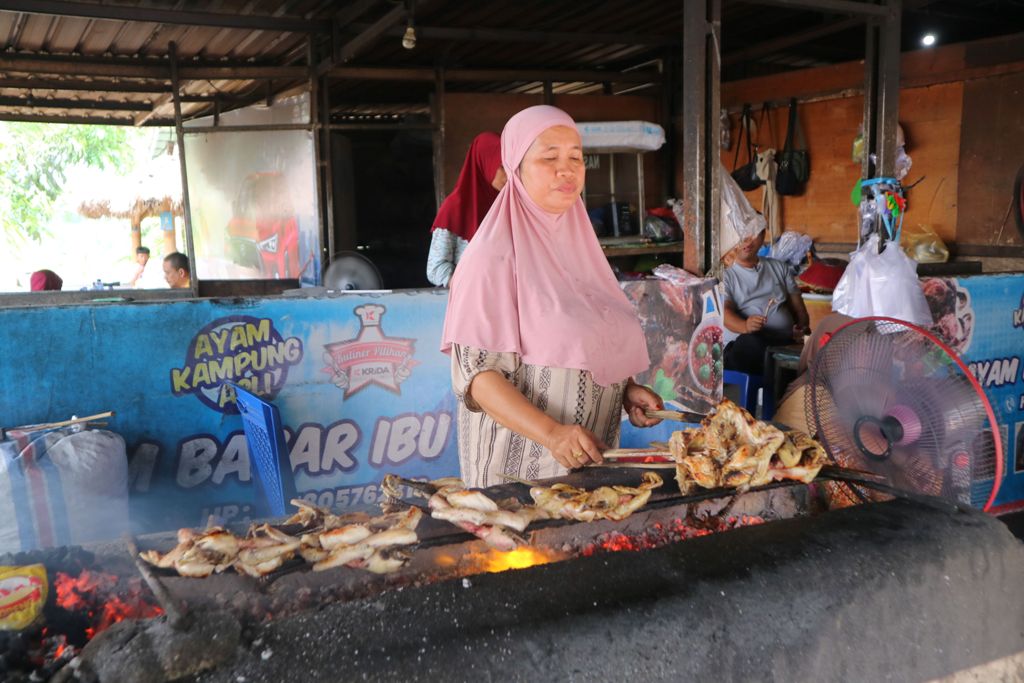 DIBURU PENGUNJUNG: Inaq Lian memanggang deretan ayam kampung yang akan disajikan pada pelanggannya di Rumah Makan Ayam Bakar Inaq Lian, Desa Sengkol, Kecamatan Pujut, Loteng.