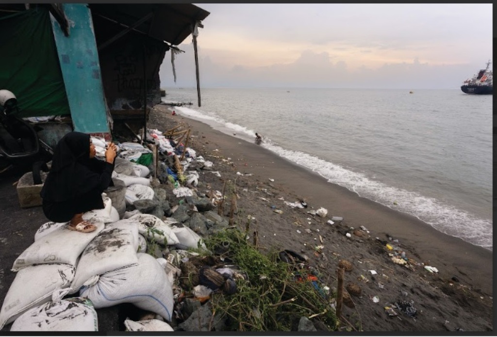 MERENUNG: Seorang warga duduk di atas karung pasir atau barikade penahan abrasi di Lingkungan Kampung Bugis, Kota Mataram, Rabu (8/1).