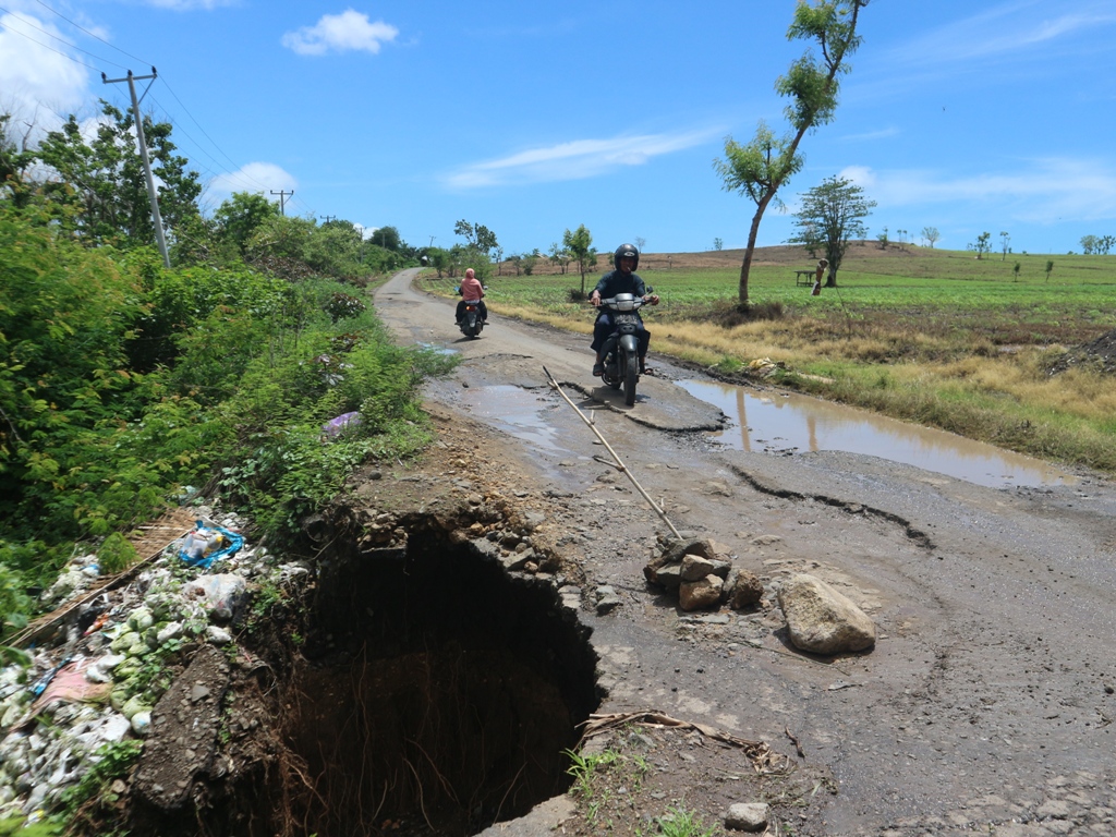 MELINTAS: Salah seorang warga Desa Sekaroh, Kecamatan Jerowaru saat melintas di jalan menuju Pantai Pink yang rusak parah.