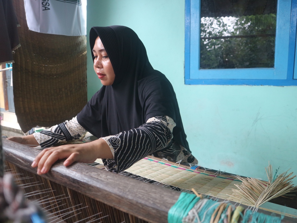 BEKERJA: Kamariah, salah satu perajin asal Dusun Paok Pondong, Desa Lenek Kecamatan Lenek saat membuat tikar mendong di rumahnya.