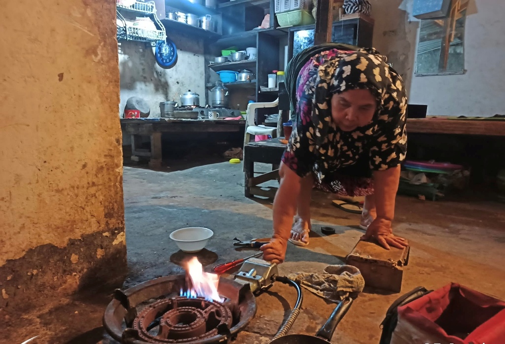 SALING MEMBANTU: Seorang lansia menyalakan kompornya setelah diperbaiki Amir, tukang servis kompor keliling.