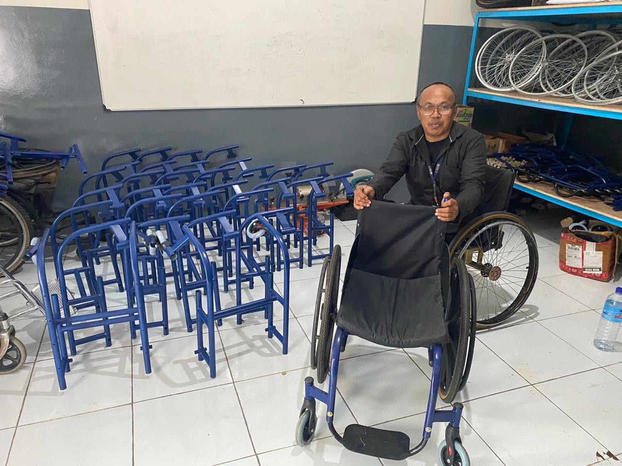 BANGGA: Lalu Wisnu Pradipta duduk di samping bahan kursi roda untuk difabel, Kamis (6/2). Bengkelnya terletak di jalan Unizar, Sandubaya, Kota Mataram.