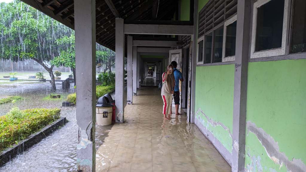 BANJIR: Seorang siswa berada di luar kelas saat hujan karena kelas mereka terpendam banjir.
