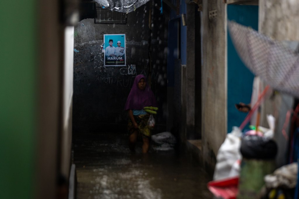 MENANTI SOLUSI: Seorang perempuan mengangkat sarungnya agar tidak basah terkena air yang menggenangi lingkungannya di Baturinggit, Kota Mataram. Warga menanti solusi jangka panjang dari Harum.