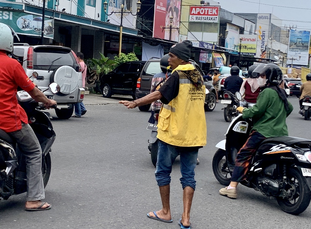 BERTUGAS: Seorang juru parkir sedang membantu pengendara untuk menyeberang di kawasan perbelanjaan Cakranegara Kamis (27/3).&nbsp;
