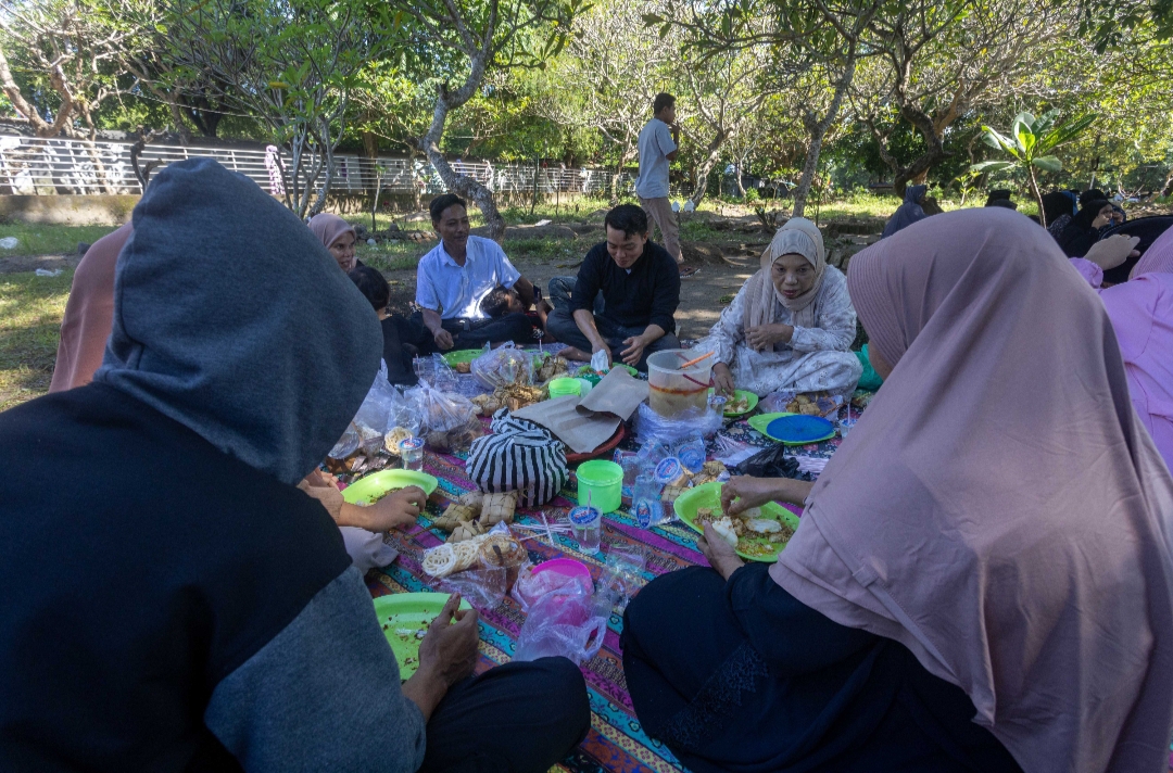 SANTAP KETUPAT: Wisatawan tengah menikamati bekal ketupat yang dibawa dari rumah di sela ziarah makam Loang Baloq , Senin (7/4/2025).