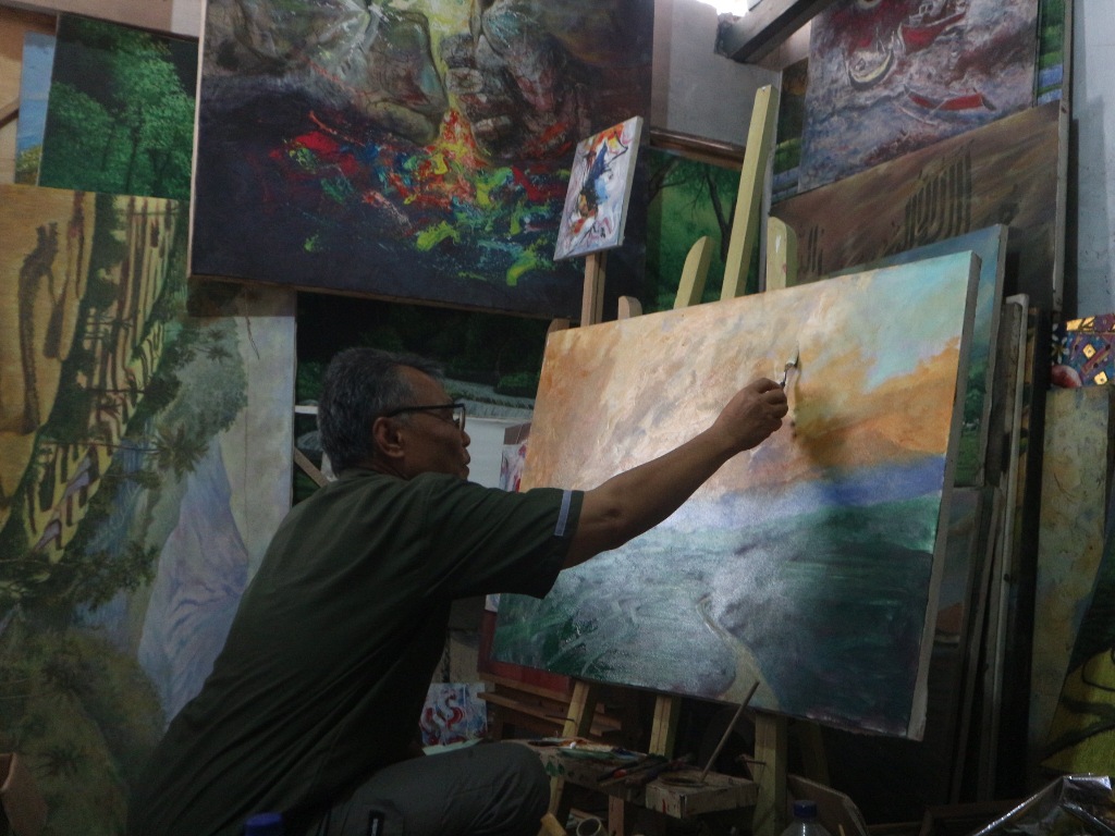 MELUKIS: Senin Apriadi saat melukis pemandangan di ruang kerjanya, Minggu (13/4).