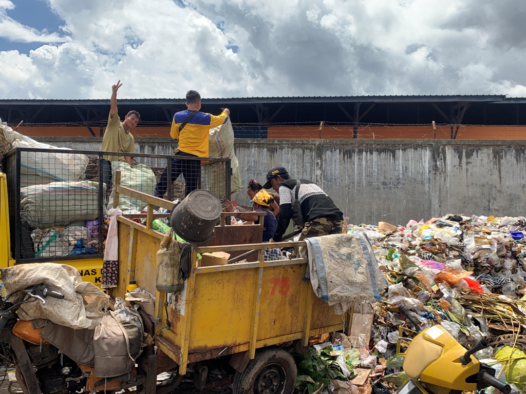 MENUMPUK : Petugas kebersihan sedang memindahkan sampah dari roda tiga ke TPS Sandubaya sembari menata tumpukan sampah agar tidak meluber keluar, beberapa waktu lalu.