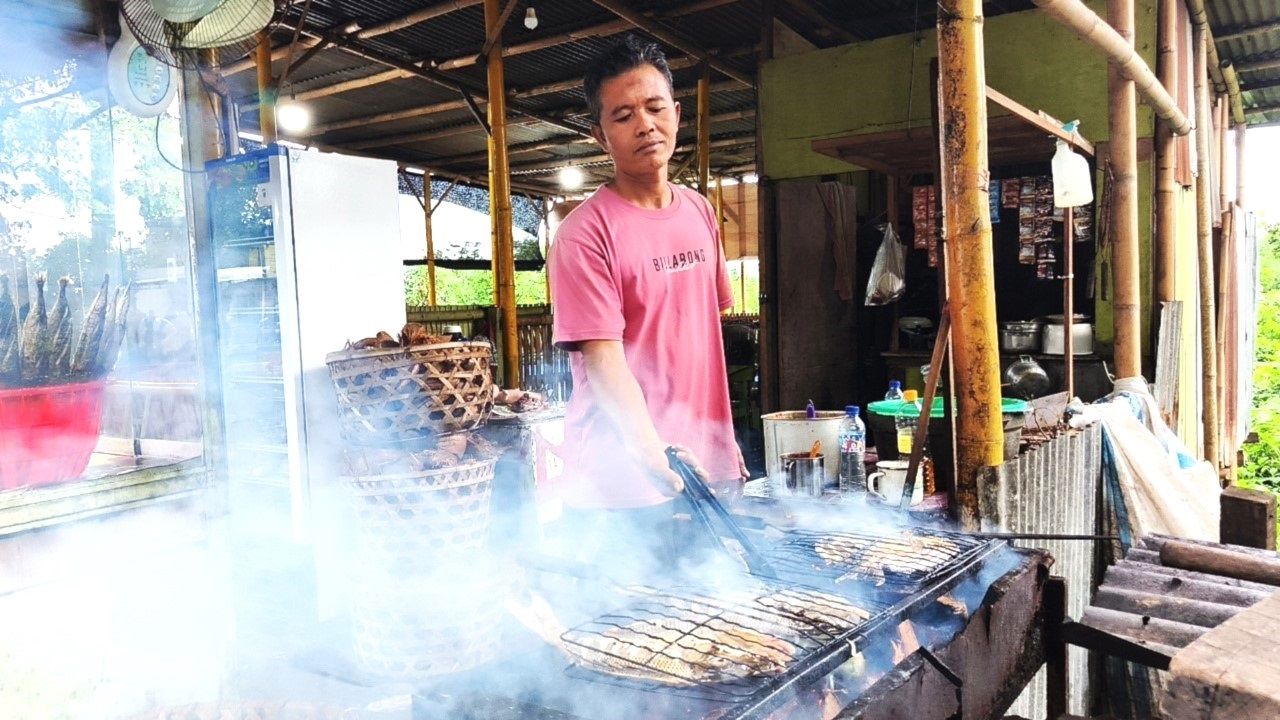 Misbah yang tengah membakar ikan pesanan konsumen di warungnya yang ada di Loang Baloq, Kota Mataram, belum lama ini.