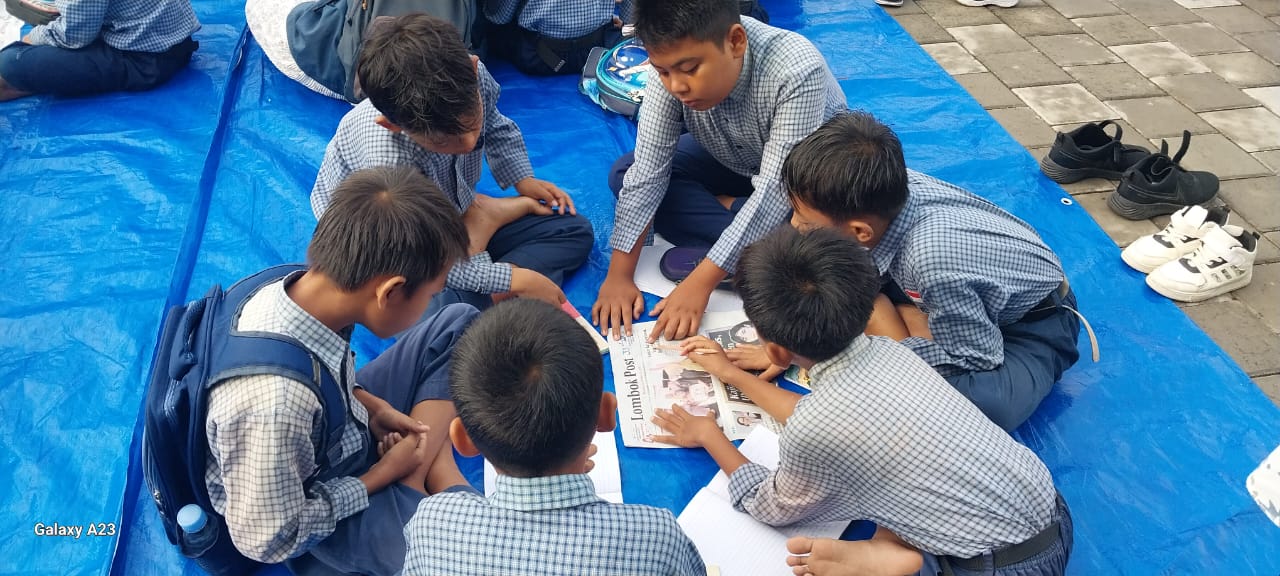 Murid SDN 32 Ampenan memanfaatkan koran sebagai media pembelajaran untuk meningkatkan literasi membaca.