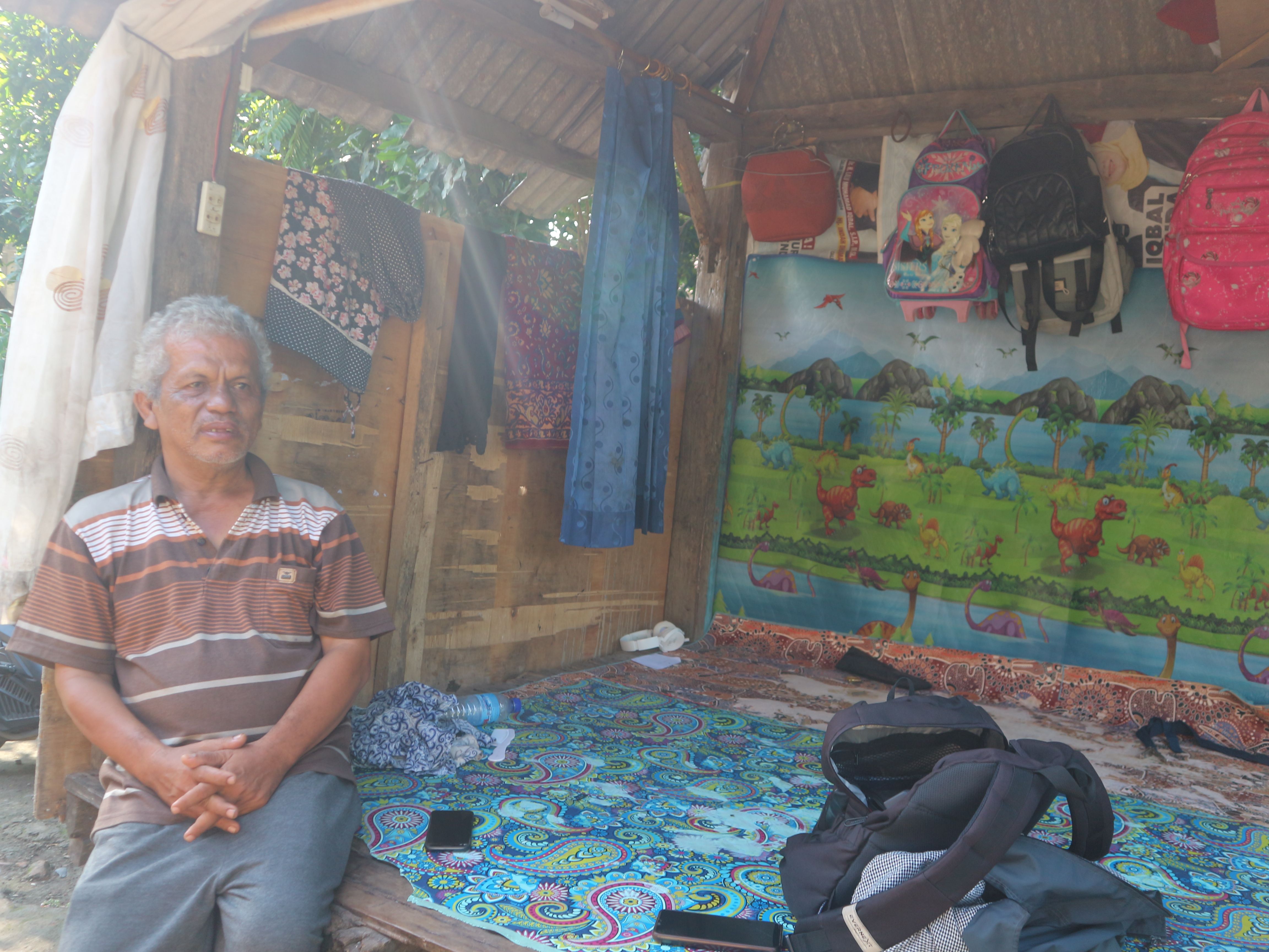 Rudi Hartawan sedang duduk di gazebo depan rumahnya yang dijadikan sebagai tempat tidur bersama istrinya.