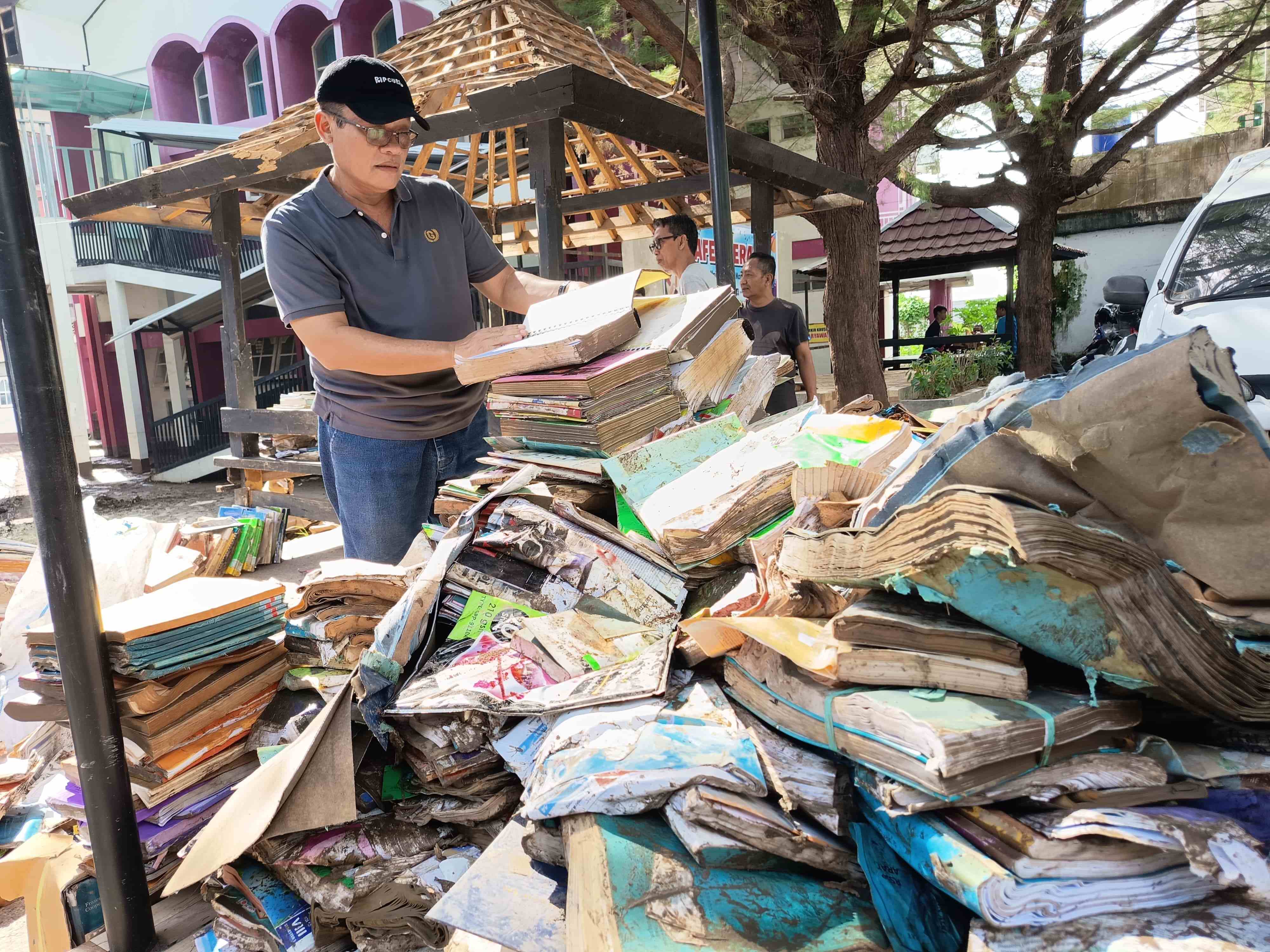 COBA DISELAMATKAN: Kepala Dinas Perpustakaan dan Kearsipan NTB H Ashari memeriksa koleksi buku yang terendam banjir, Selasa (8/7).