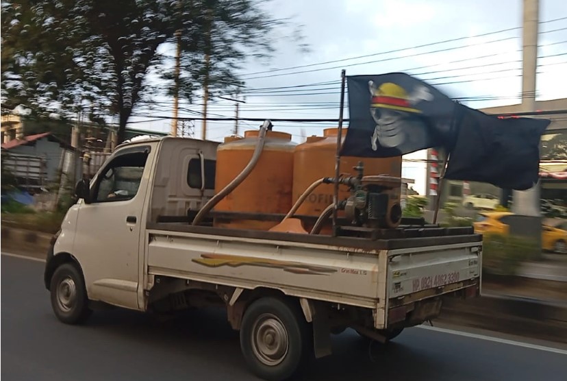 JENGAH: Salah seorang warga memasang bendera Jolly Roger dari serial kartun One Piece di mobil tempat usahanya berjualan air tandon.