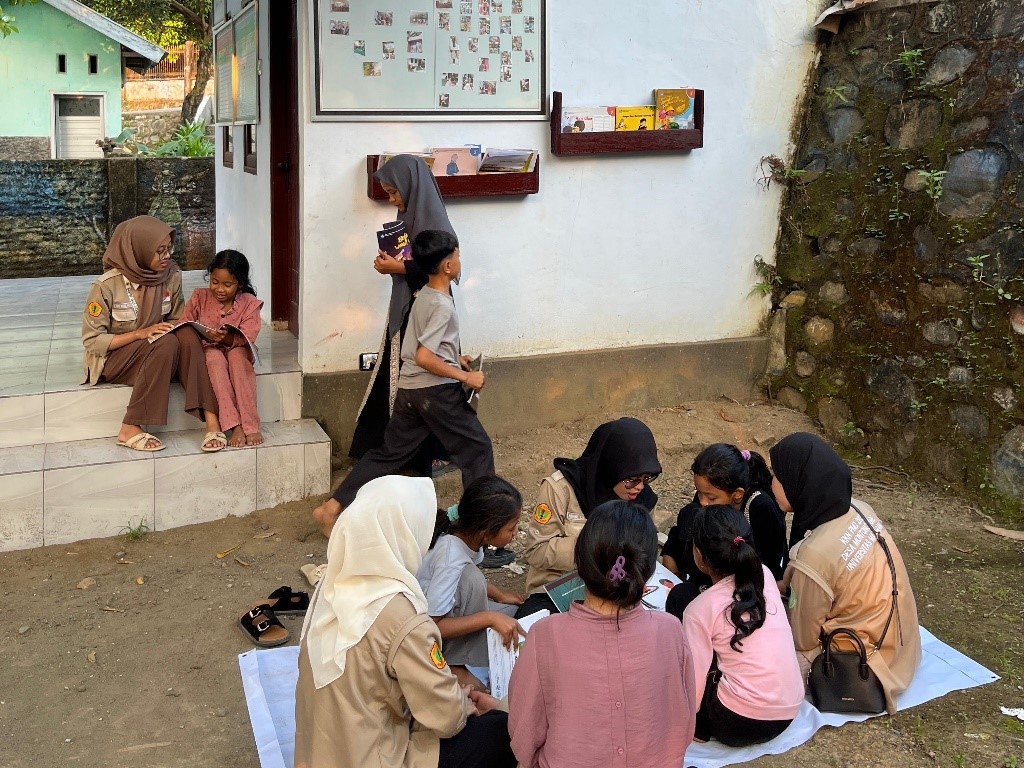 Mahasiswa KKN UNRAM membacakan cerita di Rumah Literasi Montong Are, Lombok Barat, sambil mengenalkan permainan tradisional untuk memikat minat baca anak desa.