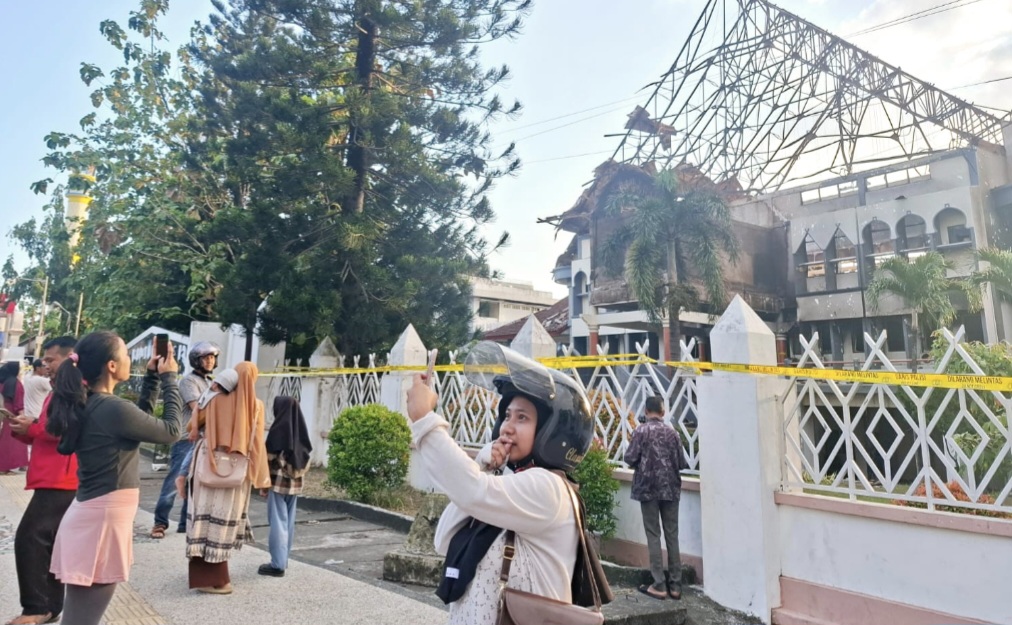 Warga dan pengguna jalan berswafoto dengan latar belakang kantor DPRD NTB yang dibakar massa aksi pada Sabtu lalu (30/8)
