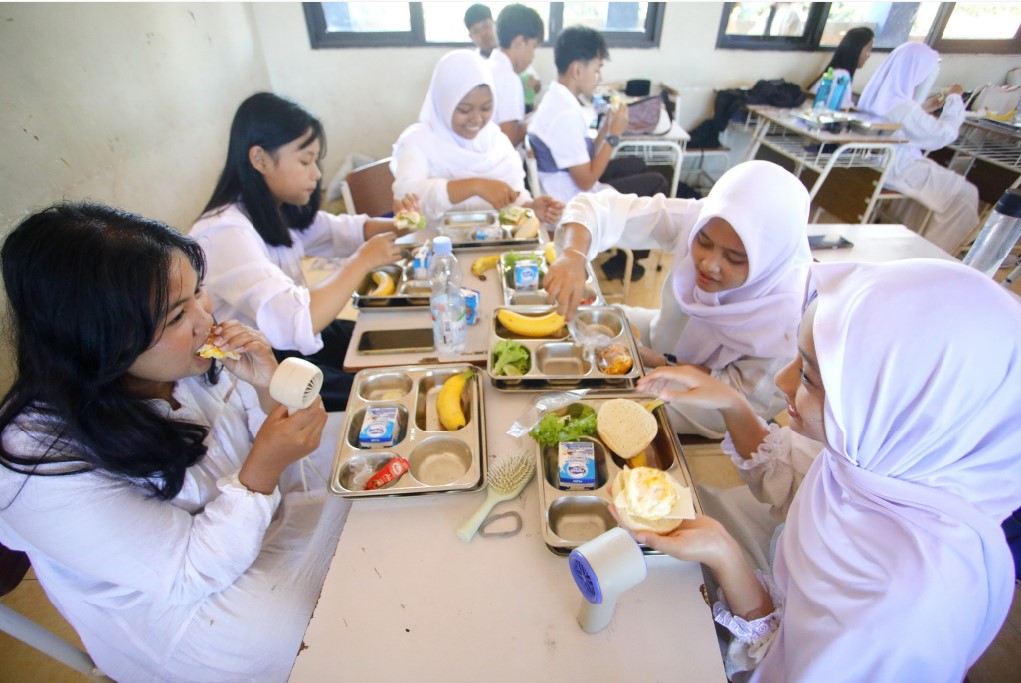PENERIMA MANFAAT: Almira Calista Medinar (kiri) dan Akila Vega (kanan), siswi kelas 10 SMAN 15 Surabaya, sedang menyantap menu makan MBG berupa burger dengan lauk telur dan keju, Jumat (19/9).