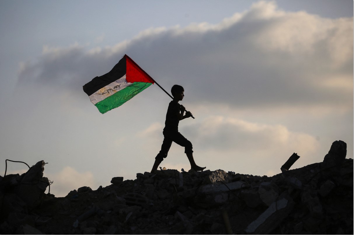 NEGARA PALESTINA: Seorang anak mengibarkan bendera nasional Palestina sambil berjalan melewati reruntuhan bangunan di kamp pengungsi Bureij di Jalur Gaza, Senin (22/9).