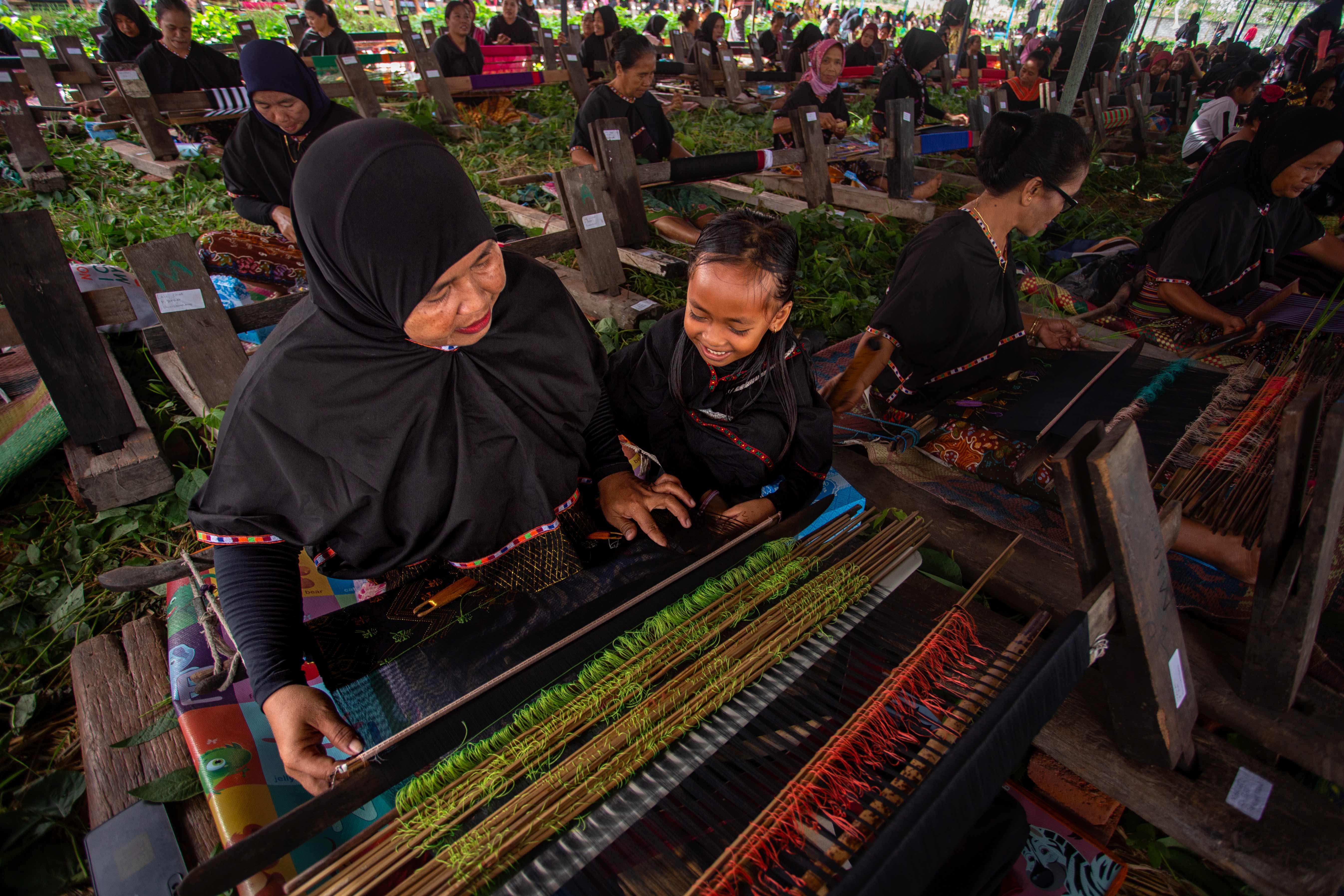 Seorang wanita mengajari anaknya cara menenun dengan alat tenun Tradisional di Desa Sukarara, Lombok Tengah.