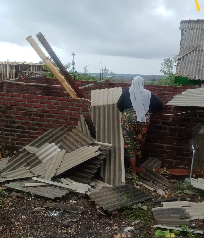 seorang warga sedang melihat kondisi rumahnya yang rusak karena diterjang angin kencang