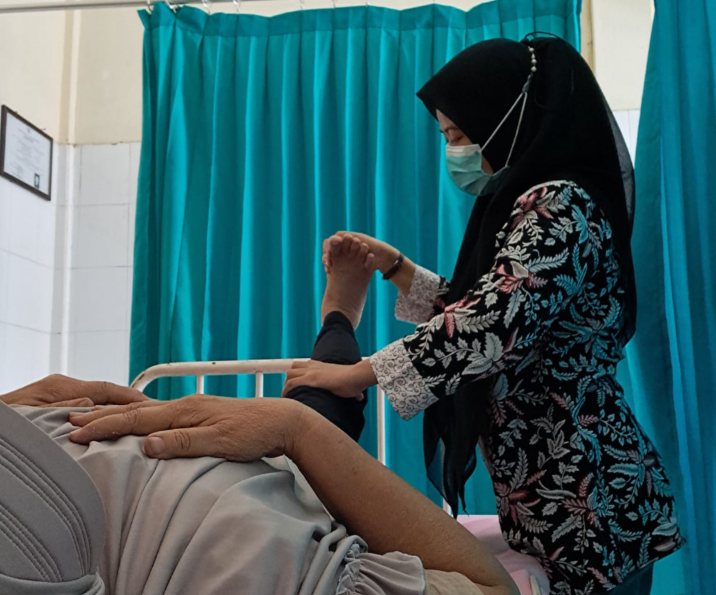 Tenaga fisioterapis membantu pasien melakukan latihan gerakan kaki untuk memperbaiki fungsi sendi dan otot.