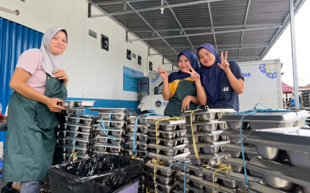 SENYUM DI ANTARA TUMPUKAN OMPRENGAN: Siti (kiri) dan Aliza (tengah), relawan pencuci piring di Dapur MBG Turida tetap bersemangat meski harus menangani ribuan omprengan setiap hari, Kamis (13/11).