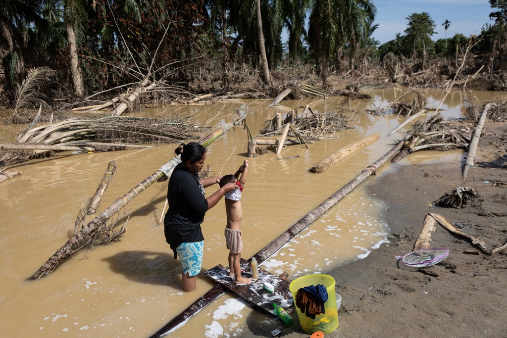 KRISIS AIR BERSIH: Seorang ibu sedang memandikan anaknya dengan air berlumpur sisa banjir bandang di samping pohon-pohon yang tumbang di Aceh Tamiang, Provinsi Aceh pada Rabu (10/12).