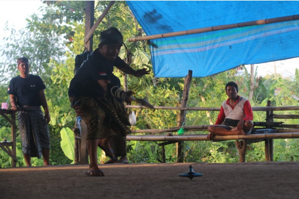 MAIN: Seorang pemain gasing sedang memutar gasingnya di tengah arena.