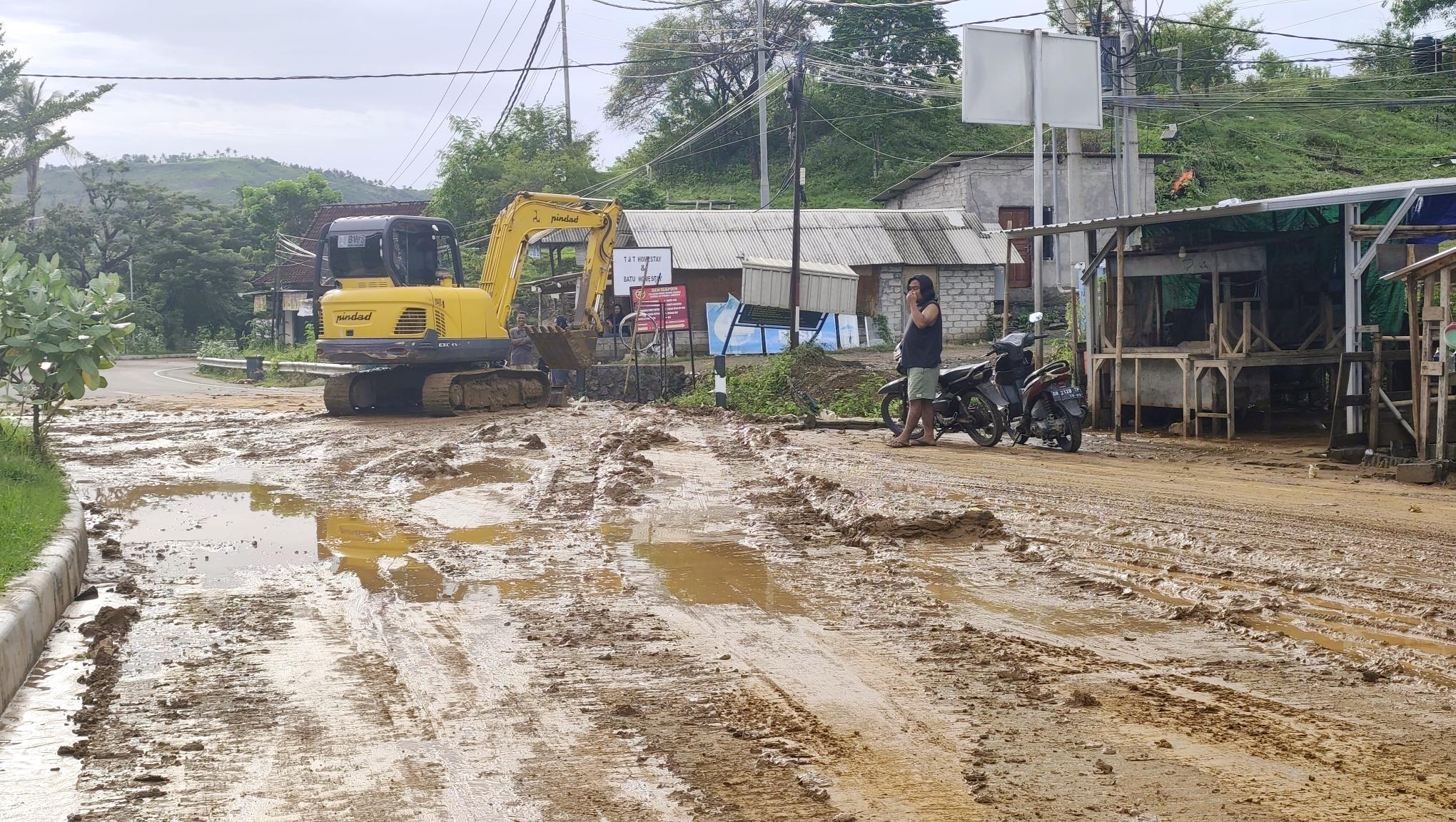 Alat berat eskavator diturunkan untuk membersihkan limpahan lumpur dari perbukitan yang terbawa saat hujan di jalan raya pariwisata Kuta Mandalika, Lombok Tengah, Sabtu (27/12).