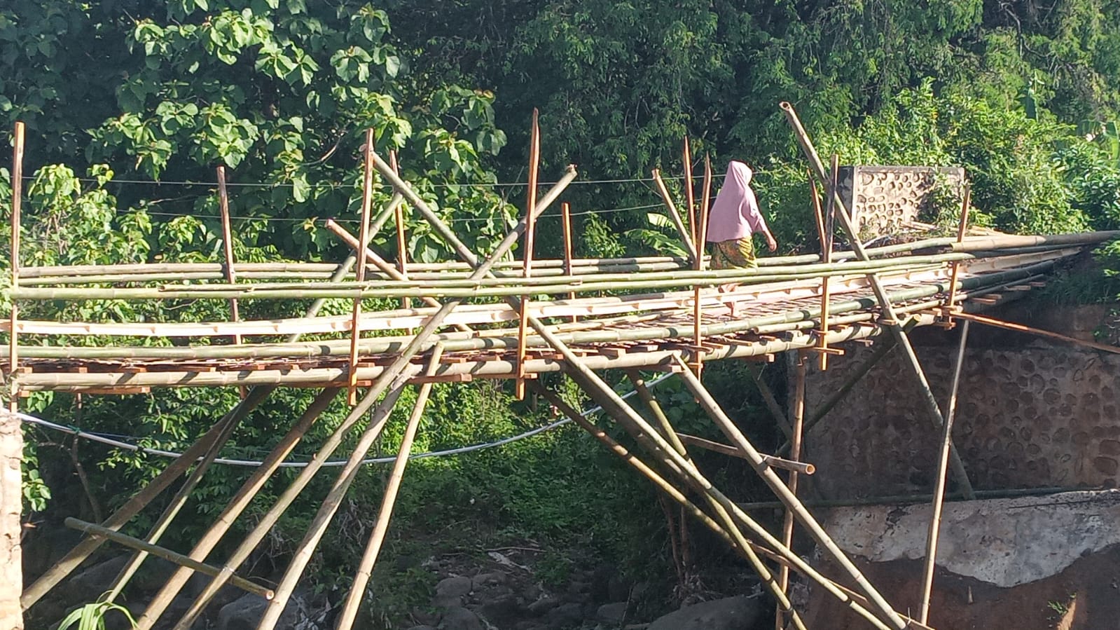Seorang warga Dusun Aik Beta Desa Perigi sedang berjalan di jembatan bambu yang dibuat secara swadaya oleh masyarakat, untuk memperlancar aktivitas sehari-hari.