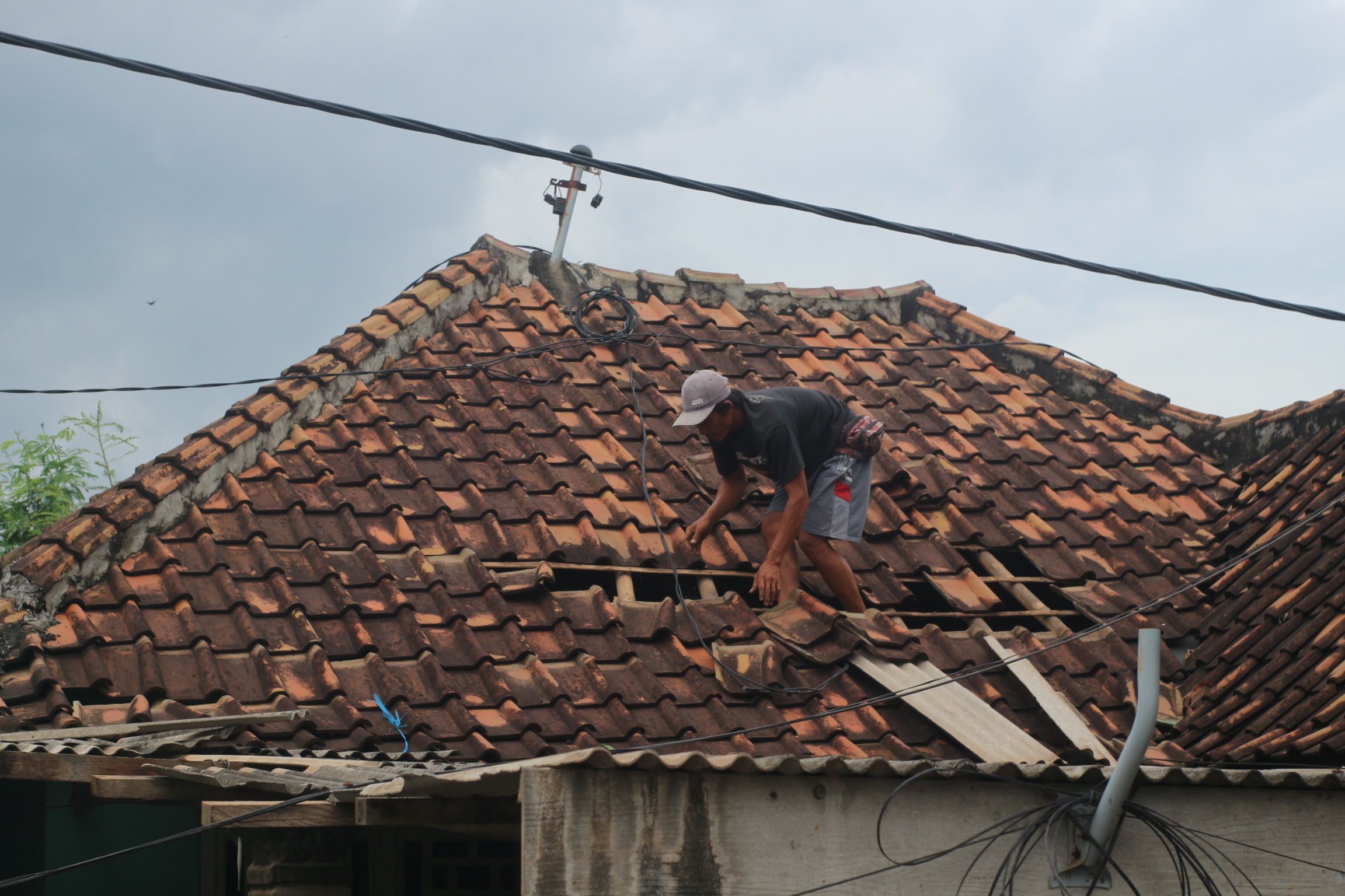 Salah seorang warga Dusun Kuwangwai, Desa Menceh Kecamatan Sakra Timur saat memperbaiki atap rumahnya yang diterbangkan oleh angin kencang pada Minggu (11/1)