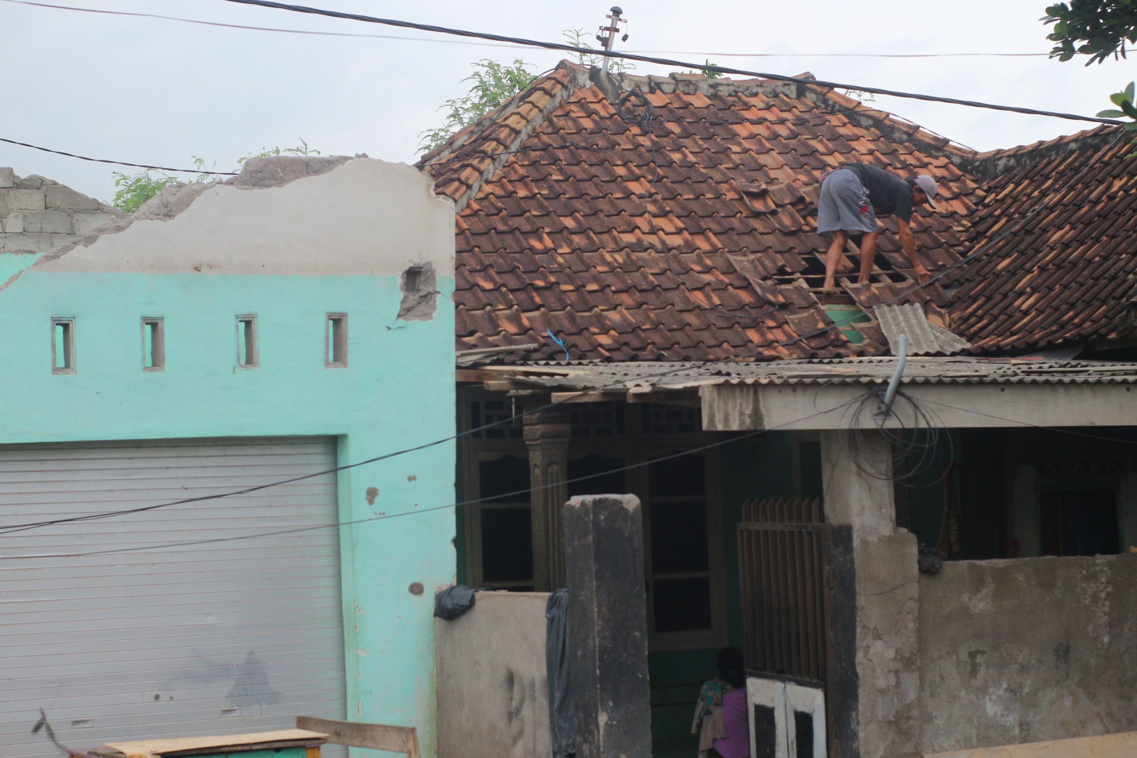 Seorang warga Dusun Kuwangwai Desa Menceh saat memperbaiki genteng rumah yang roboh.