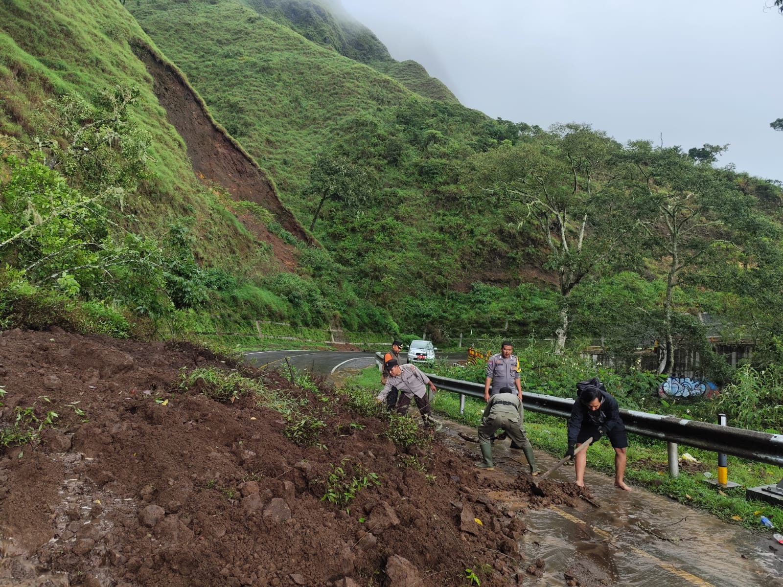 Petugas kepolisian bersama TNI, Satpol-PP saat membersihkan material longsor yang menutupi badan jalan menuju Pusuk Sembalun