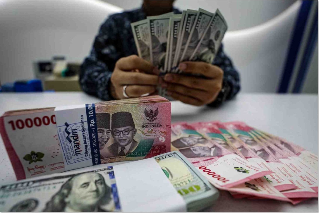 TERUS MELEMAH: Pegawai salah satu bank menunjukan mata uang Dolar Amerika dan Rupiah.