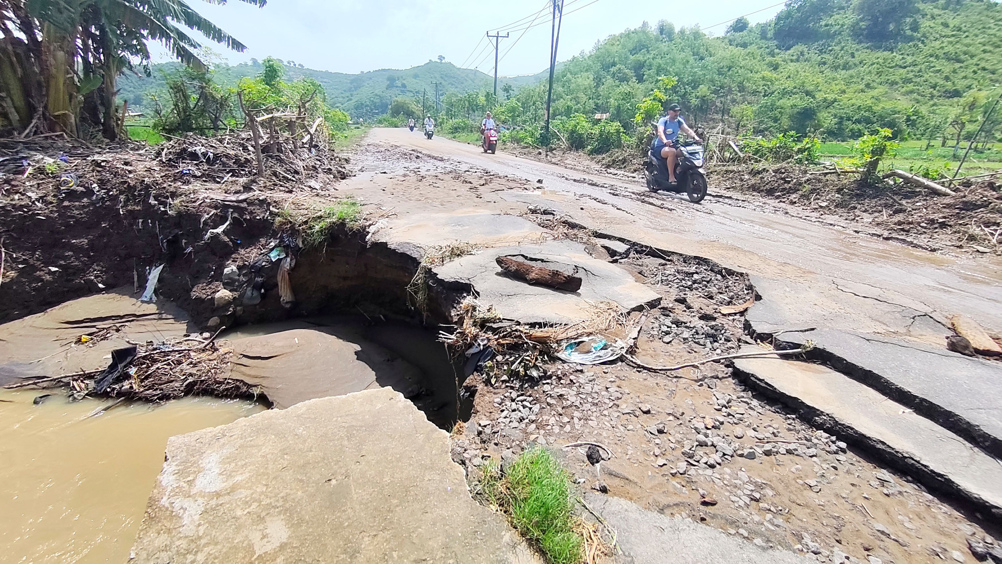 Sejumlah turis melintas di atas jalan raya Selong Belanak-Mawun yang nyaris putus usai diguyur hujan lebat beberapa hari lalu, Jumat (23/1).