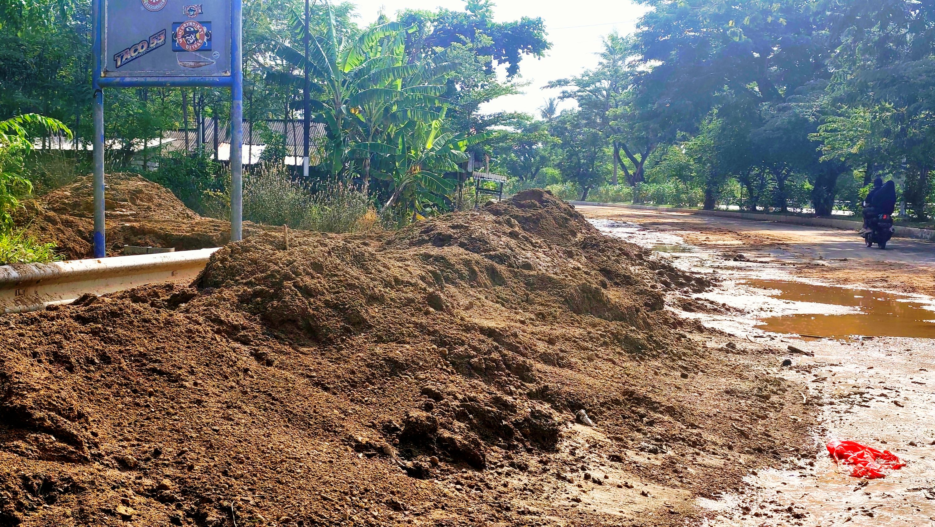 Pengendara bermotor melintasi gundukan lumpur dari perbukitan yang turun ke Jalan Raya Sengkol atau depan Sirkuit Internasional Mandalika, Desa Kuta, Pujut, Lombok Tengah, Minggu (25/1).