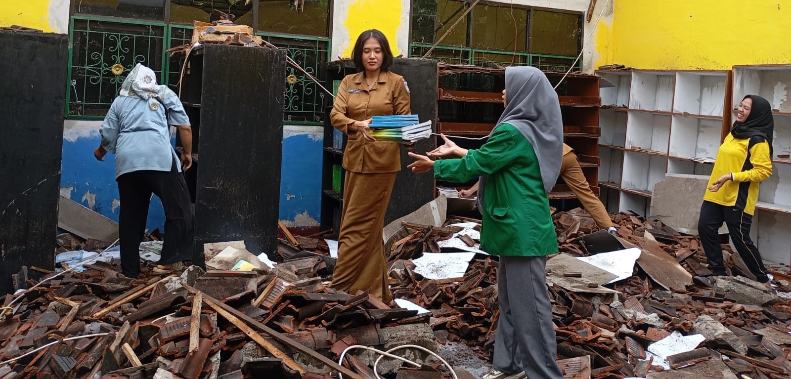 Guru SMPN 14 Mataram menyelamatkan buku di Ruang Perpustakaan yang atapnya ambruk akibat cuaca ekstrem, Selasa (27/1).