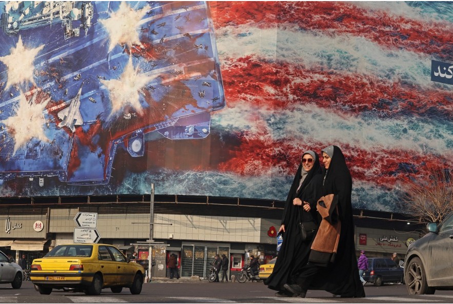 PANAS: Wanita Iran berjalan melewati papan reklame anti-AS yang terpasang di sebuah gedung di Lapangan Enqelab di Teheran, Senin (26/1).