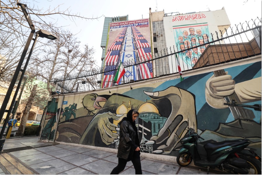 KIAN PANAS: Seorang wanita Iran berjalan melewati spanduk anti-AS dan anti-Israel yang tergantung di sebuah gedung di Lapangan Palestina di Teheran, Selasa (27/1).
