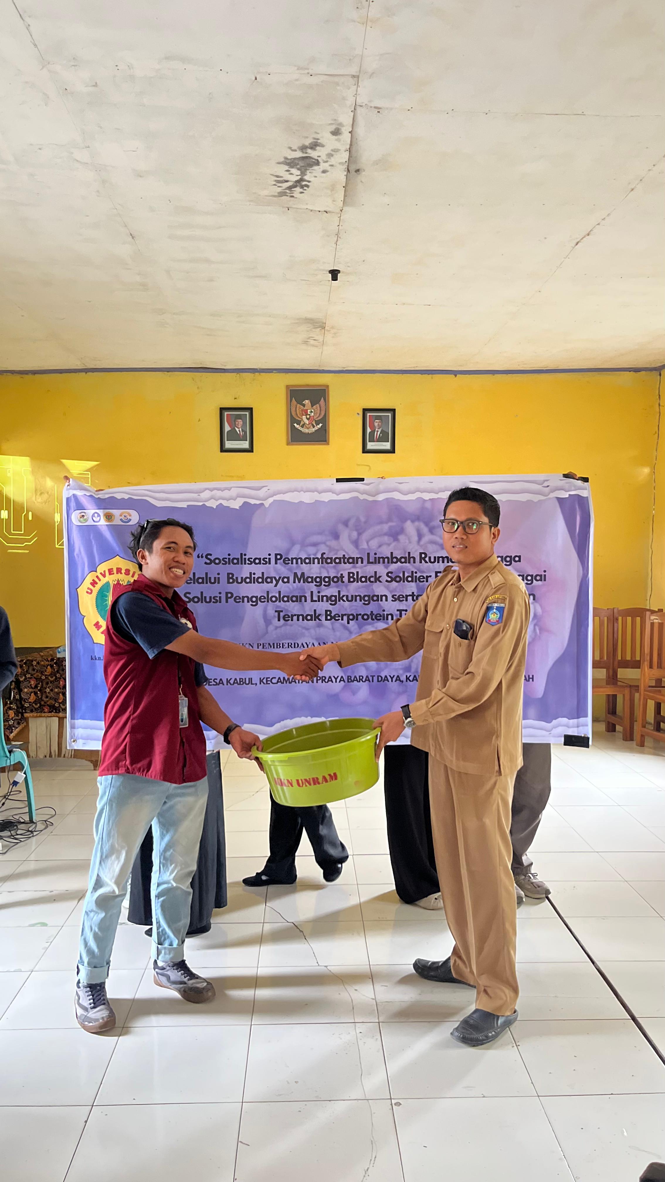 SOSIALISASI: Perwakilan mahasiswa KKN Unram (kiri) Desa Kabul juga menyerahkan kandang maggot sederhana secara simbolis kepada Sekdes Desa Kabul