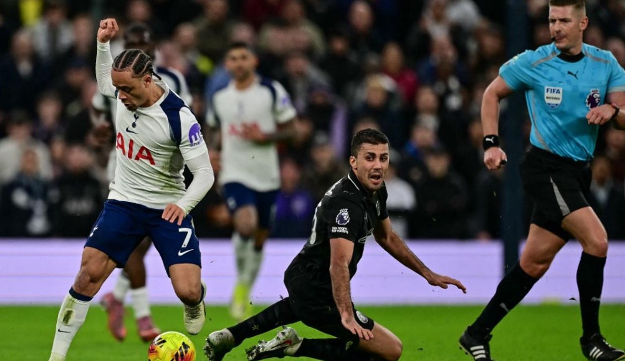 Wasit mengamati benturan antara gelandang Tottenham Hotspur Xavi Simons (kiri) dan gelandang Manchester City  Rodri (tengah) dalam pertandingan di Stadion Tottenham Hotspur, London. (Ben STANSALL/AFP)