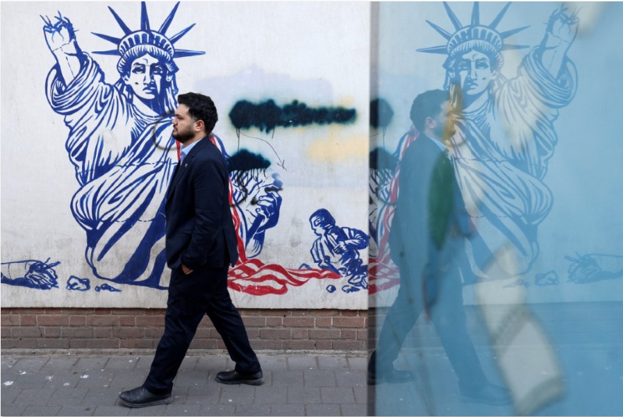 KIAN PANAS: Seorang wanita berjalan melewati mural yang menggambarkan pesawat tak berawak AS yang dilukis di dinding luar bekas kedutaan besar Amerika Serikat di Teheran pada Minggu (1/2).