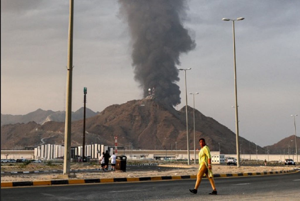 TERDAMPAK: Seorang wanita menyeberang jalan yang di belakangnya tampak kepulanan asap tinggi membubung setelah ledakan di zona industri Fujairah, Uni Emirat Arab, Selasa (3/3). 