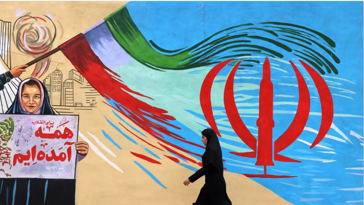 TAK GENTAR: Seorang wanita Iran berjalan melewati mural anti-AS dan anti-Israel di Teheran, Selasa (21/4). Gencatan senjata selama dua minggu antara Iran dan AS akan berakhir hari ini. Namun putaran kedua negosiasi terancam tertunda. (ATTA KENARE / AFP)