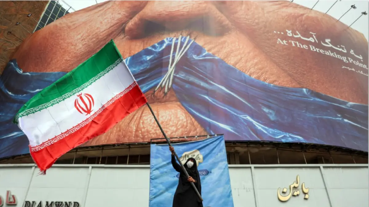 SIMBOL PERLAWANAN: Seorang wanita memegang tiang bendera Iran di depan papan reklame anti AS di Lapangan Valiasr, Teheran, Minggu (10/5). (AFP)