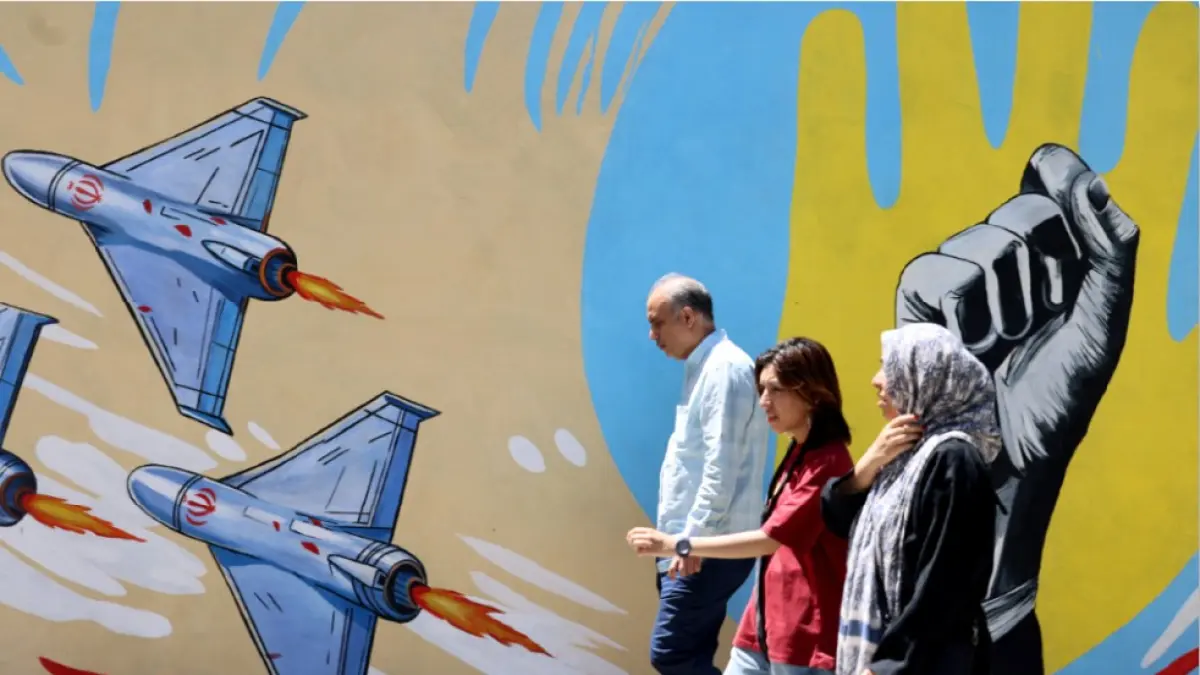 SIAP TEMPUR: Warga Iran berjalan melewati mural anti-AS dan anti-Israel yang dilukis di dinding di ibu kota Teheran pada Ahad (10/5) lalu. Pemerintah Iran melatih warganya menggunakan senjata untuk mengantisipasi perang lanjutan melawan Amerika Serikat dan sekutunya Israel. Persiapan ini dilakukan Pemerintah Iran menyusul masih buntunya negosiasi dengan Amerika Serikat. (ATTA KENARE / AFP)